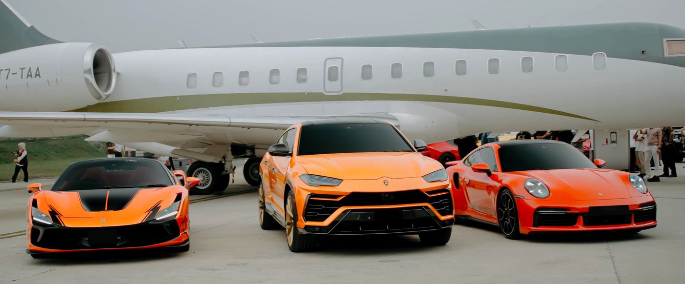 Orange Ferrari F8, Lamborghini Urus and Porsche 911 Turbo S in front of a private jet